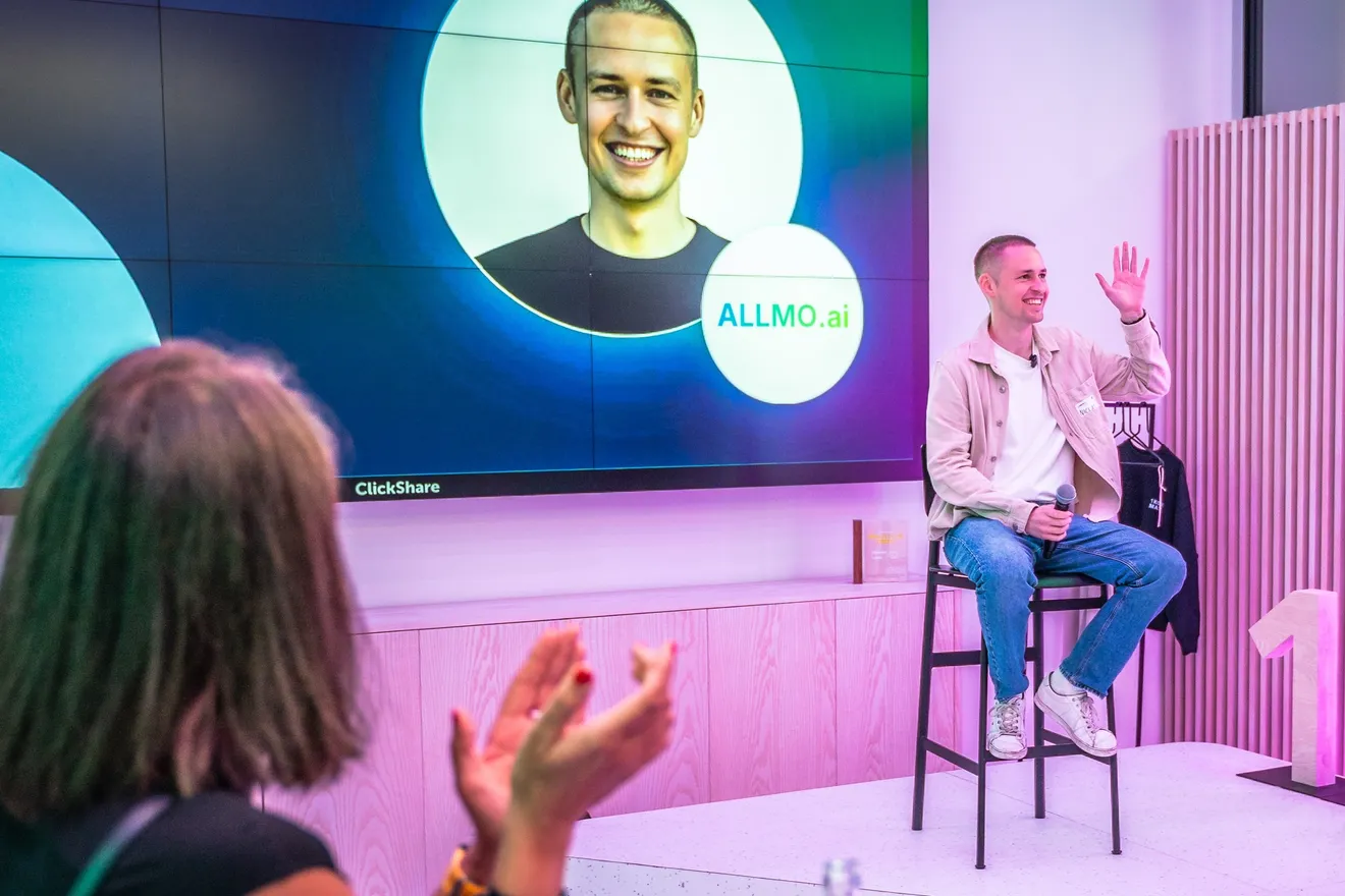 Niclas Aunin on stage at a Hamburg event, waving with a microphone in hand, in front of a screen showing his portrait and the ALLMO.ai logo.